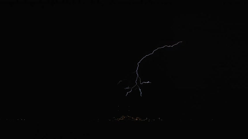 A lightning strike pierces through dark stormy skies illuminating the landscape below