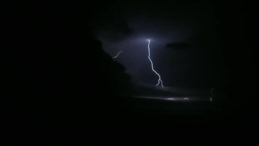 A lightning strike pierces through dark stormy skies illuminating the landscape below