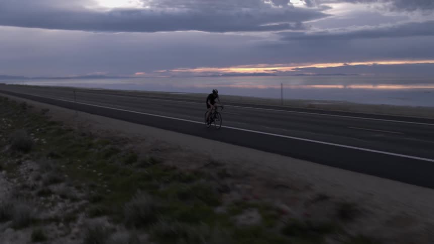 A man is racing his bicycle down the road at sunset