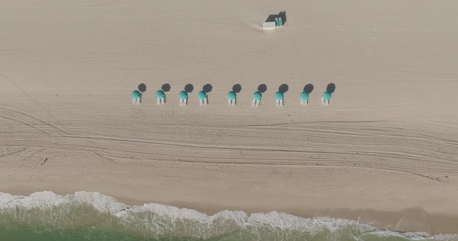 Aerial view of a serene sandy beach with blue umbrellas waves gently lapping at the shore