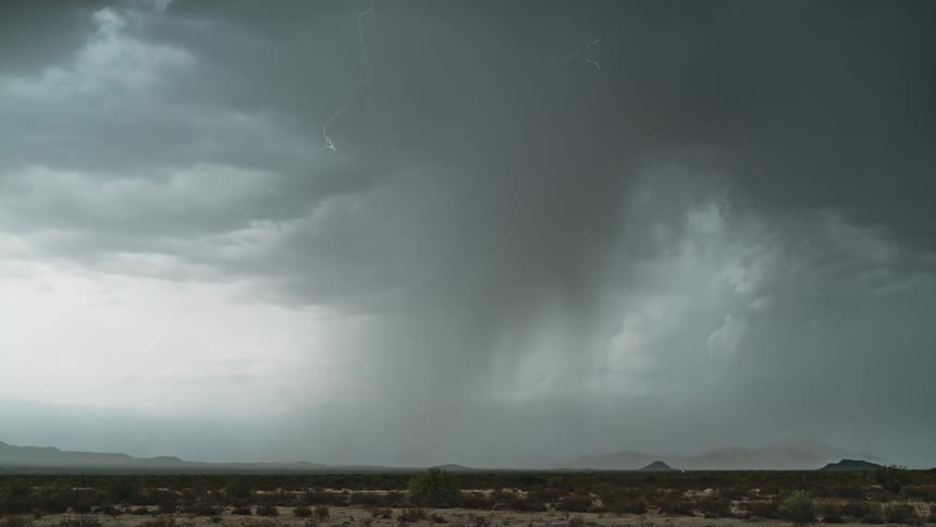 A dark storm tosses lightening around the sky over mountains and a desert