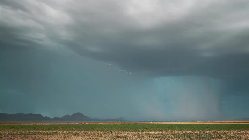 A lightning strike pierces through dark stormy skies illuminating the landscape below