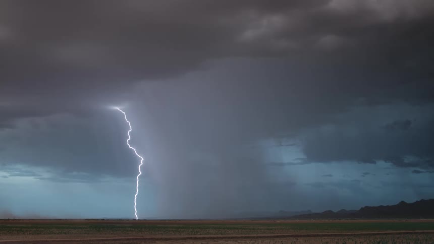 A lightning strike pierces through dark stormy skies illuminating the landscape below