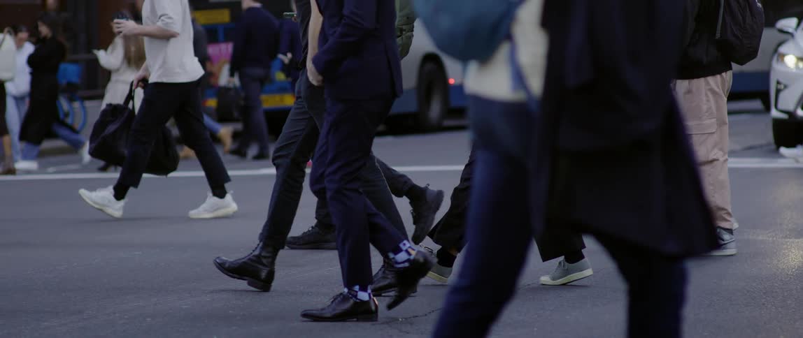 Several pedestrians are crossing an asphalt street and there is a repaired white car behind a white stripe
