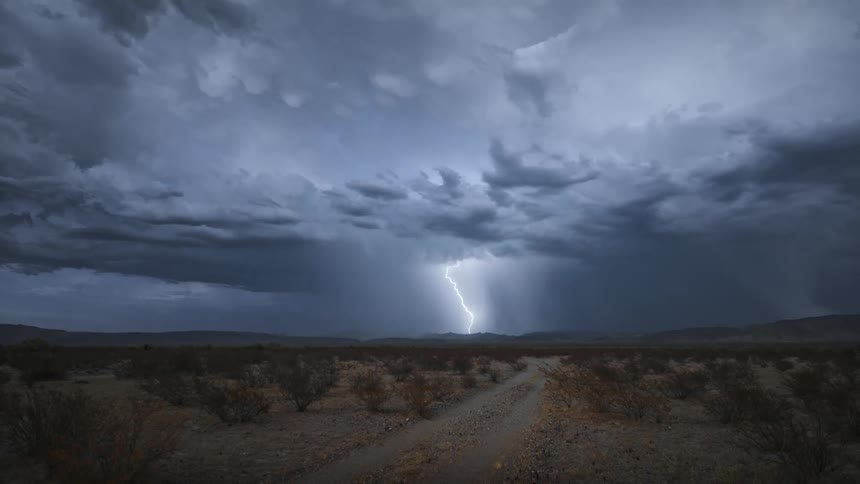 Huge lightning strikes fall from dark storm clouds over mountains and a desert