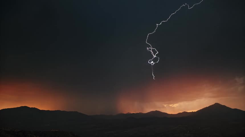 Very active lightning storm in dark clouds over mountains at sunset