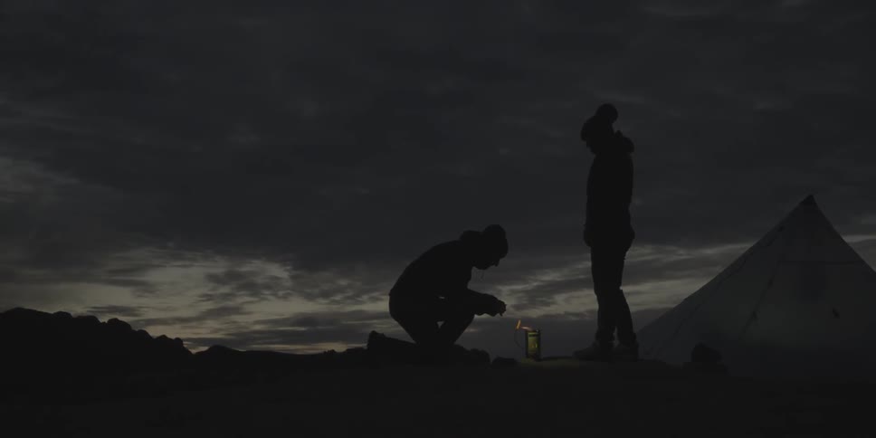 Two people are setting up a camp at night