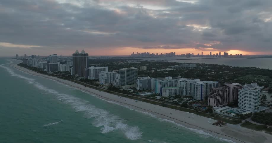 An aerial view of a coastal city at dusk with the sun setting over the skyline
