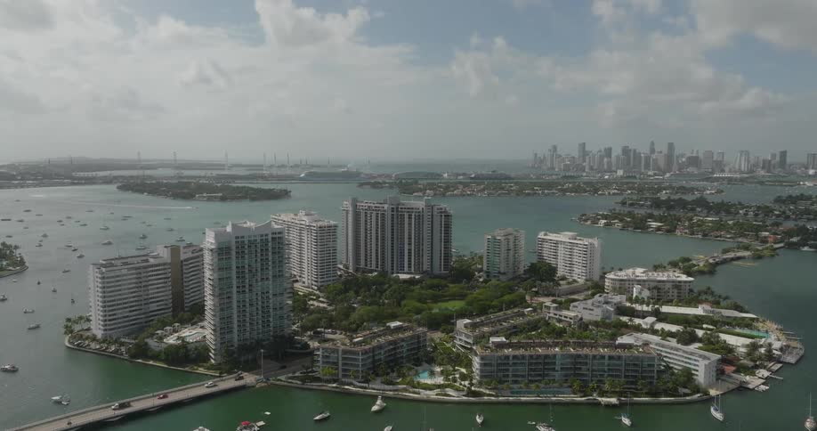 A coastal cityscape with high rise buildings near the waters edge and sailboats scattered in the bay