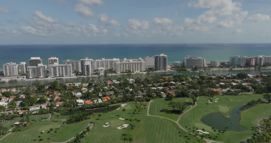A golf course and a neighborhood sit across the river from a city in front of the ocean
