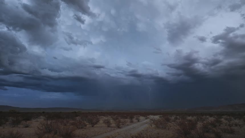 Lightning strikes near the mountains on the horizon during a thunderstorm over arid scrub land