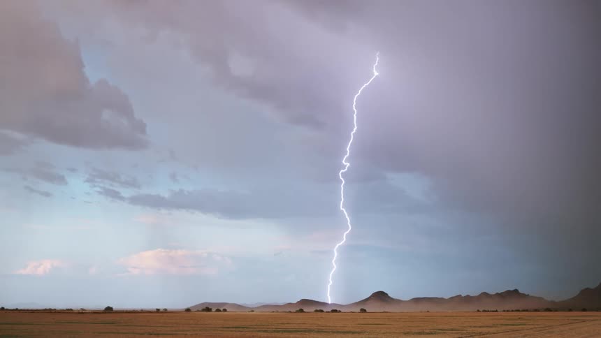 Lightning strikes hills between the snowy mountains and the grassy plains during a thunderstorm