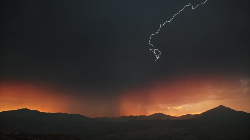 Lightning storm covers the mountains as the sun sets