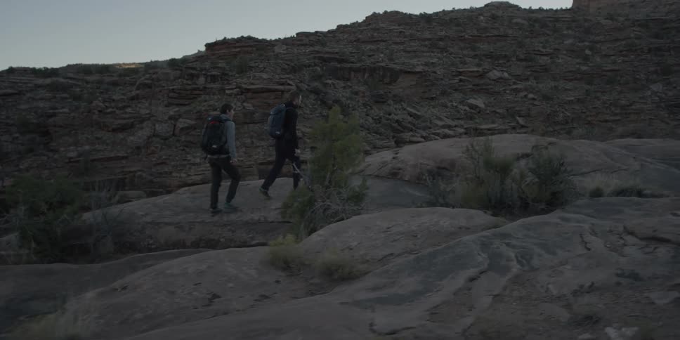 Two people hiking up rocky terrain in wilderness