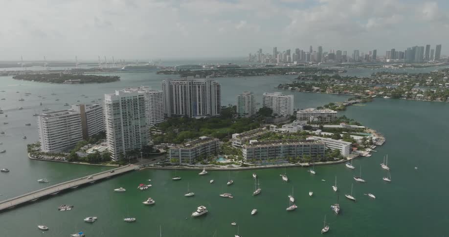 A coastal cityscape with high rise buildings near the waters edge and sailboats scattered in the bay
