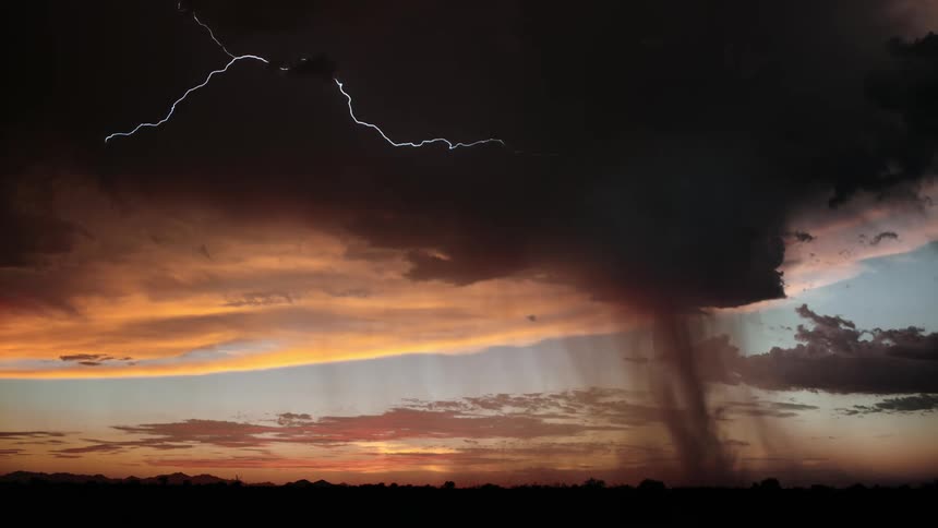 A tornado touching down near the horizon under a stormy sky with visible lightning at sunset