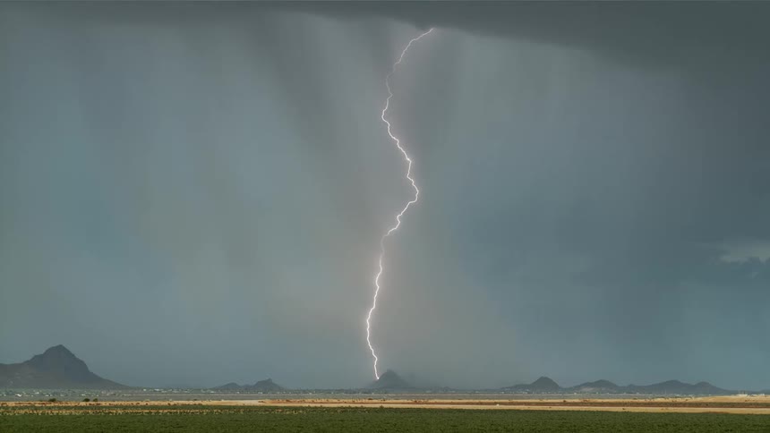 Several massive bolts of lighting travel from the storm clouds above to the landscape below