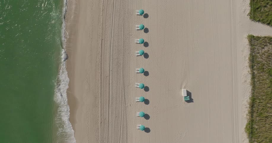 View from above of an umbrella on the sand of a beach with greenish waters