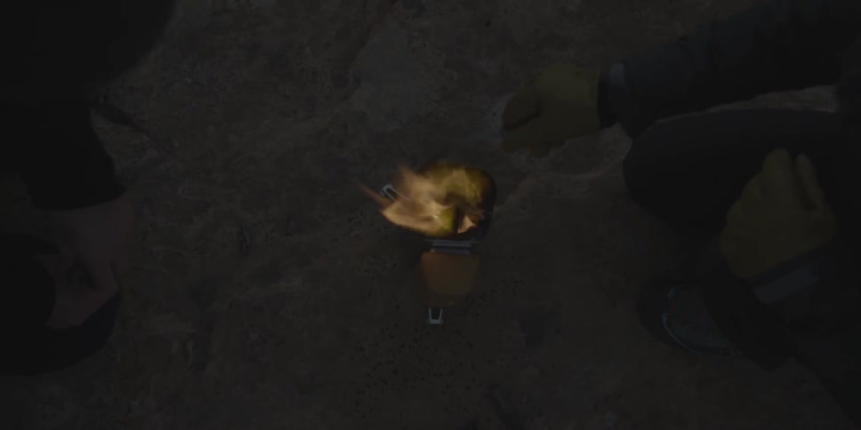 A person pokes at a small fire burning in a canister at night