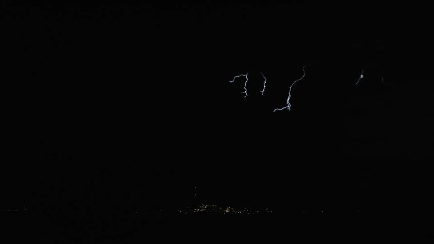 A lightning strike pierces through dark stormy skies illuminating the landscape below