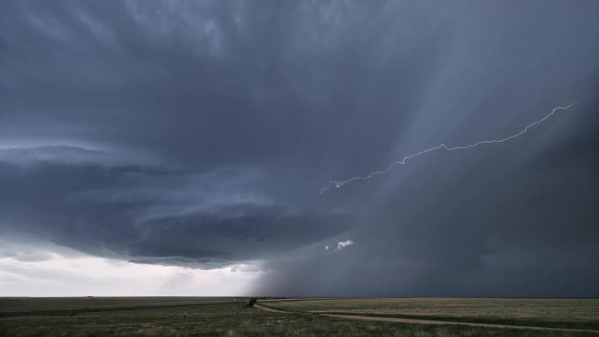 A lightning bolt cutting through a dark swirling storm cloud over a flat open field