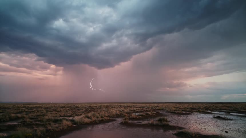 A lightning storm tearing up the sky with a dark cloud in a flat region