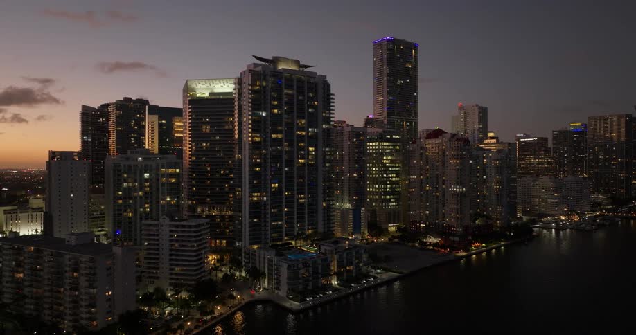 A city skyline at twilight featuring illuminated highrise buildings against the fading sky