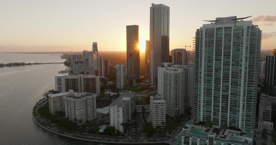 Aerial scene of large modern buildings by the sea and the sun on the horizon