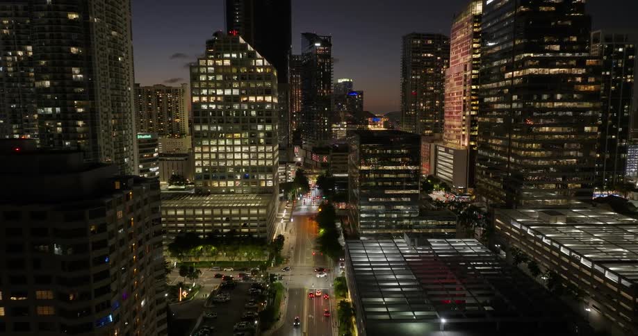 A city skyline at twilight featuring illuminated highrise buildings against the fading sky