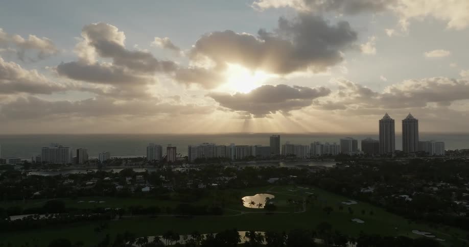 A city skyline with tall buildings against a backdrop of a sunset or sunrise next to the ocean