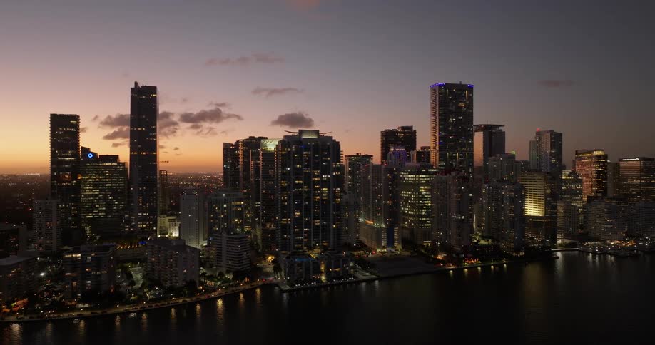 A city skyline at twilight featuring illuminated highrise buildings against the fading sky