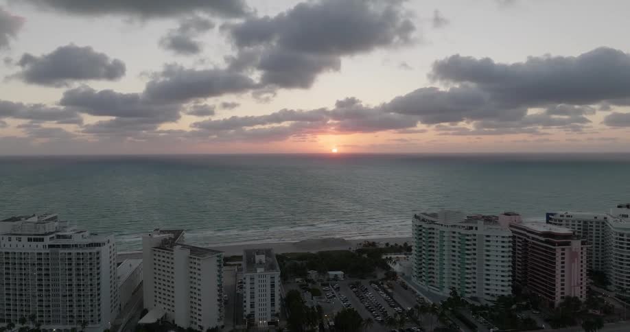 A coastal cityscape at sunset featuring highrise buildings along the shore