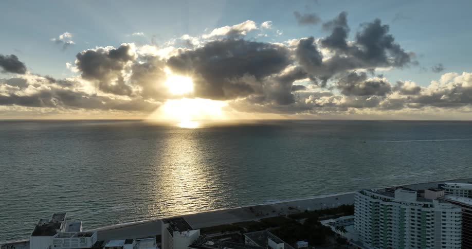 Sunlight shines through clouds above the ocean next to a coastal city