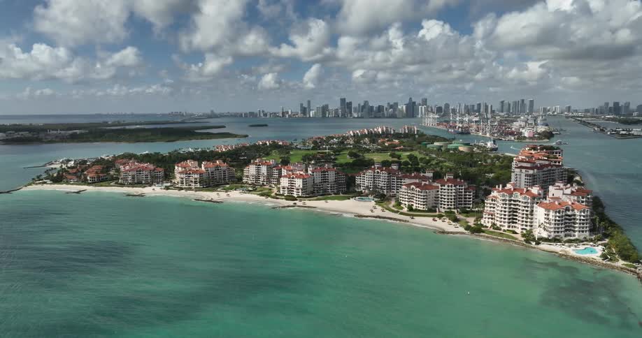 A large island with several resort buildings facing the sea and in the background there is a city with tall buildings