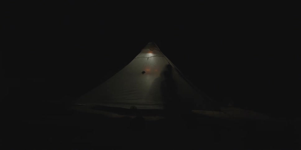 A person adjusts a light inside a tent at night time