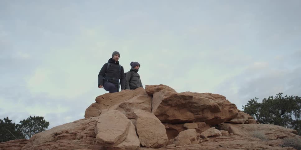 Man and woman hiking up onto rocks then stopping to observe surroundings