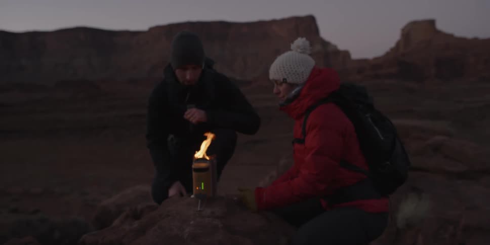 People sitting around a small fire outdoors on a cold evening in the wilderness
