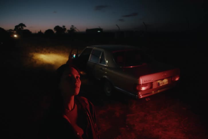 Woman stands in a field near parked car and looks toward the sky at night