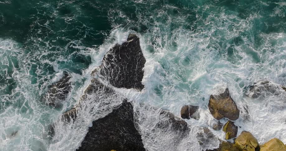 Ocean waves crash against rock formations and boulders on the coast