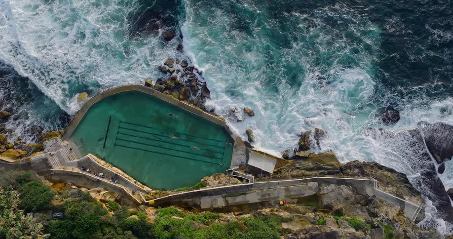 Waves crash against the base of cliff near a swimming pool
