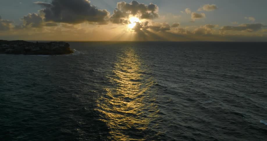 A serene sunset over the ocean with golden reflections on the water and partly obscured clouds