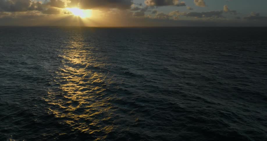 The sun about to set above a calm ocean hidden by clouds