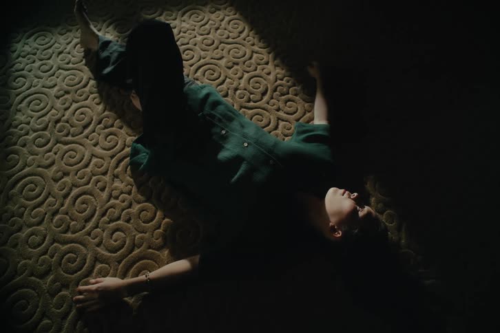 An woman lays on a carpeted floor in a dark room