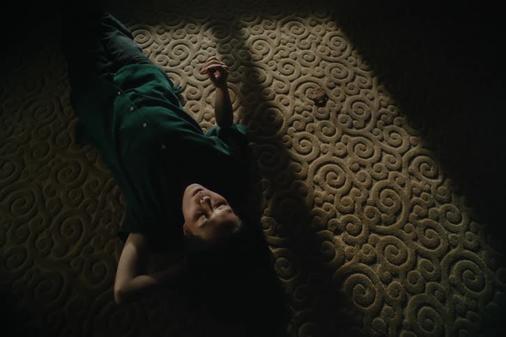 Woman chews while lying on the carpet in a shadowed room