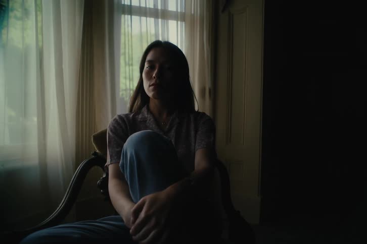 A woman sitting in a chair in a room looks up at the ceiling