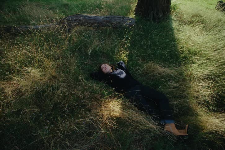 A woman lying on tall grass relaxing under the shadow of a tree