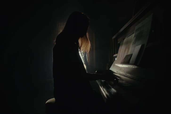 Silhouette of a woman sitting and playing the piano in a dark room