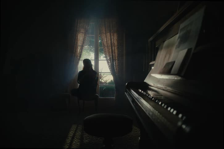 A woman sitting in a dark room with a piano looking out the window