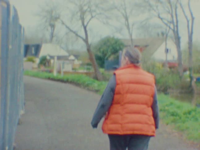 Person in an orange jacket walking down a street in an urban neighborhood