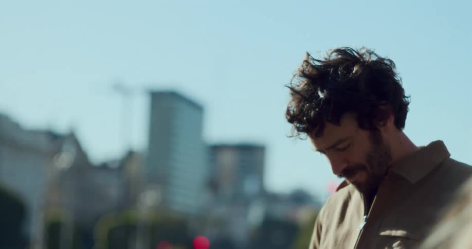 A man with a beard is looking down and there is a blurred woman in front of him